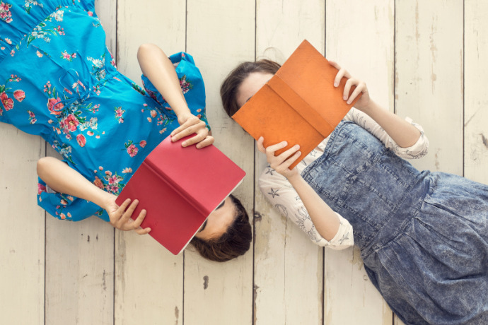 Duas mulheres deitadas sobre a madeira lendo um livro