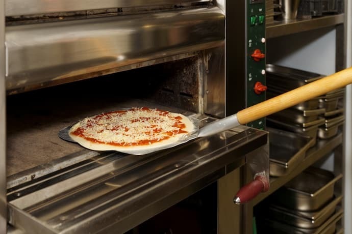 Pizza sendo colocado no forno com a ajuda de uma pá de pizza