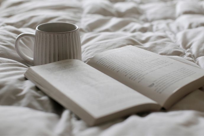 Copo de café e livro aberto na cama