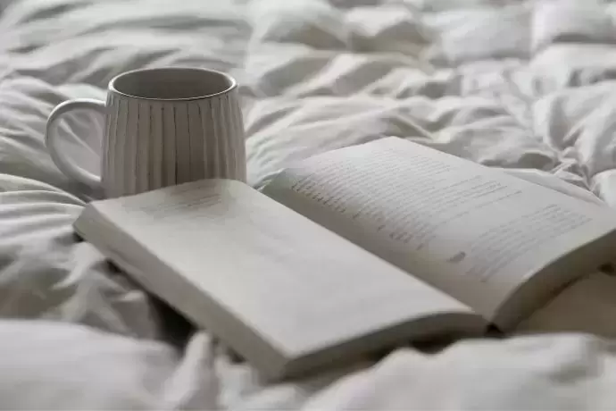 Xicara de café e livro aberto na cama