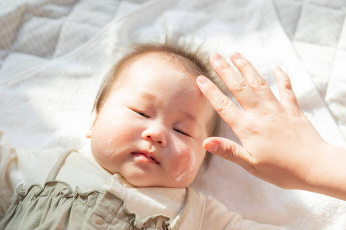 Pessoa passando hidratante infantil em rosto de bebê