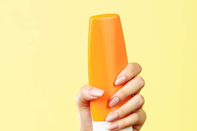 Mão feminina segurando frasco de protetor solar