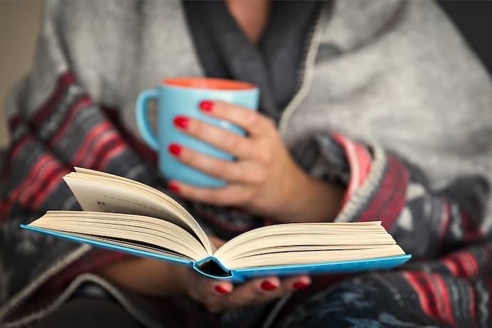 Pessoa lendo livro e tomando café