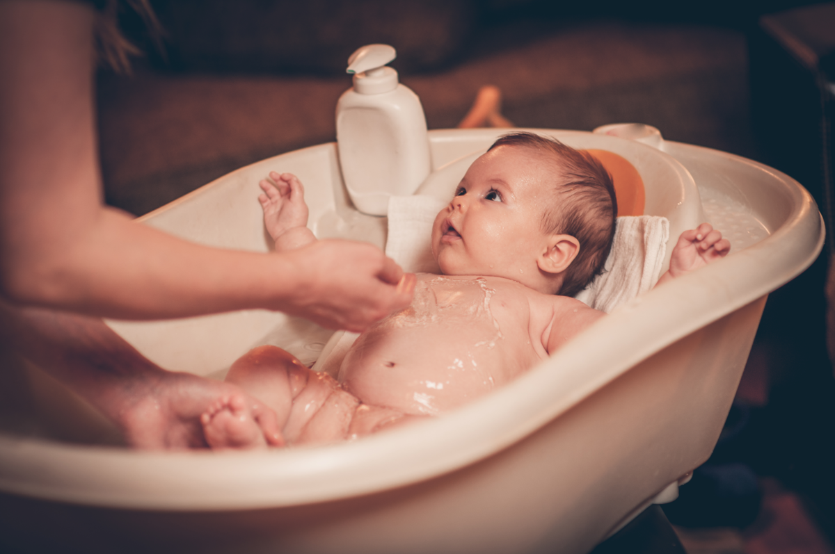 bebê na banheira com adulto dando banho