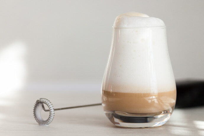 Espumador de leite e um copo de café com leite espumado