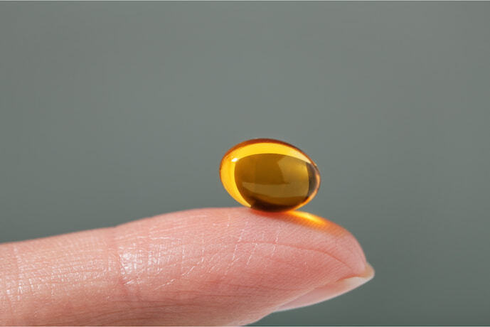 Cápsula de vitamina apoiada em um dedo.